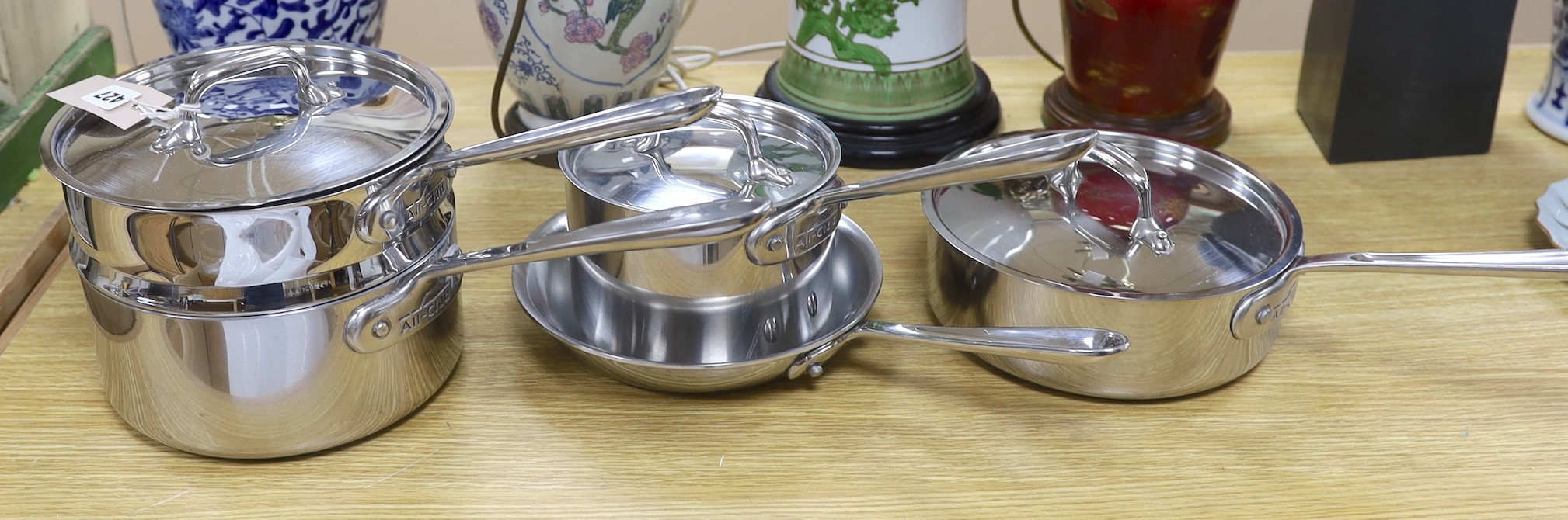 An “All Clad”, stainless steel steamer saucepan and cover, two other saucepans and covers and a matching frying pan, steamer 16cms high
